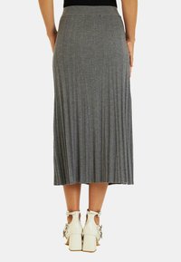 Jupe midi grise côtelée avec une taille élastique, ornée de plis verticaux. Assortie à des chaussures à talons blocs blanches avec des embellissements.