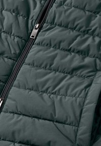 Donzen jas in donkergroen, met een doorgestikt ontwerp, een gladde textuur en een zilveren ritssluiting aan de voorkant.