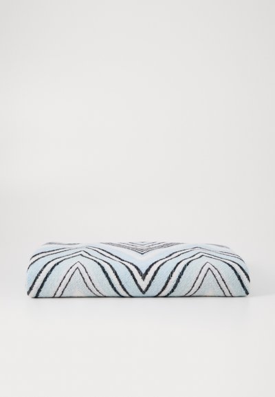 Kudottu viltti, jossa on chevron-kuvio vaaleansinisissä, mustissa ja valkoisissa sävyissä. Pehmeä tekstuuri suorakulmaisen muotoisena.