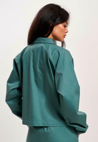 Teal kurz geschnittene Jacke mit glatter Textur, lässiger Passform und klassischem Kragen. Mit fallenden Schultern und langen Ärmeln.
