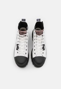 Zapatillas altas con un cuerpo de lona blanca y una puntera de goma negra. Cuenta con cordones blancos, un collar acolchado y suela texturizada. Logo horizontal.