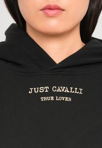 Hoodie noir avec une coupe décontractée, arborant un texte crème "JUST CAVALLI TRUE LOVER" brodé sur la poitrine et une texture douce.