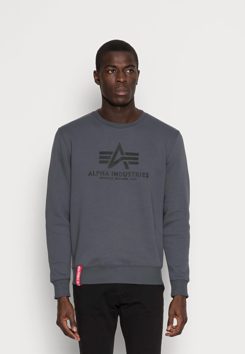 Sudadera gris hecha de mezcla de algodón, con un logo negro en el pecho, puños acanalados y una etiqueta roja en el dobladillo. Diseño de ajuste casual.