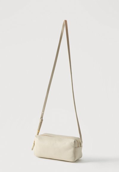 Μικρή ορθογώνια τσάντα crossbody από μπεζ δέρμα με μακρύ ρυθμιζόμενο λουράκι και χρυσό φερμουάρ, απεικονίζεται σε απλό λευκό φόντο.