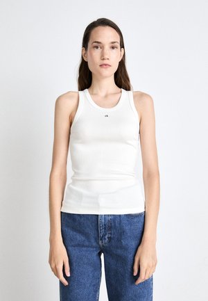 Débardeur blanc à côtes avec un col rond et un petit logo noir "ck" au centre. Associé à un jean taille haute bleu.