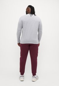 Grå langermet genser med rund hals, kombinert med burgunder tapered joggebukser. Grå sneakers vises delvis ved føttene.