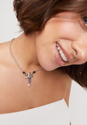 Collar de cadena de plata con un colgante de libélula que presenta cuentas azules y plateadas, textura suave y una mezcla de acabados brillantes y mate.