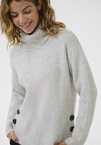Pilkos tekstūruotos, su raukiniais, turtleneck tipo megztinis su laisvu siluetu, šone turintis du tamsiai rudos spalvos mygtukus.