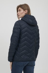 Doudoune bleu marine avec un motif en chevrons, dotée d'une capuche et d'un design matelassé. Fabriquée en tissu brillant et léger.