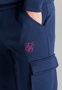 Marina cargo-byxor av slät tyg; har en sidficka och en rosa broderad logga. Funktionell design med strömlinjeformad silhuett.