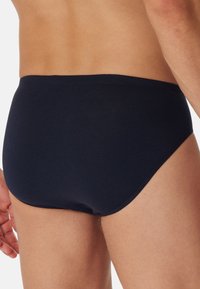 Marineblaue Badebriefs mit einer glatten, weichen Textur. Der mittelhohe Schnitt hat einen regulären Bund und bietet umfassende Abdeckung im Rückenbereich.