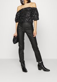 Mustat paljetti off-the-shoulder -paita puffitaskuilla, yhdistettynä korkeavyötäröisiin mustiin nahkahousuihin ja mustiin korkeakorkoisiin nilkkabootseihin.