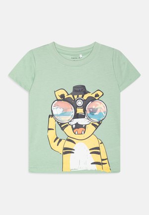 Camiseta de manga corta verde claro con un gráfico de un tigre amarillo que lleva gafas de gran tamaño y un sombrero negro, con rayas en blanco y negro.