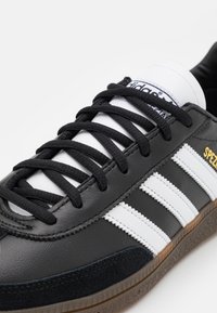Czarno-biały sneaker Adidas z czarnymi sznurowadłami, trzema białymi paskami po bokach oraz złotym napisem "SPEZIAL" blisko podeszwy.