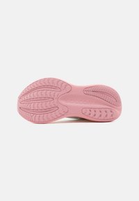 Ρόζ σόλα παπουτσιού τρεξίματος Saucony με υφή για καλύτερο κράτημα και το εμπορικό σήμα χαραγμένο στο κέντρο, σε λευκό φόντο.