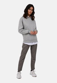 Sivá mikina s okrúhlym výstrihom, vrstvená nad bielou košeľou s golierom, v kombinácii so slim-fit béžovými nohavicami a bielymi teniskami.