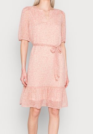 Kobieta ubrana w jasnoróżową sukienkę w kwiaty z krótkimi bufkami na rękawach, paskiem przewiązanym w talii, dekoltem w serek i falbaną u dołu, sięgającą nad kolana.