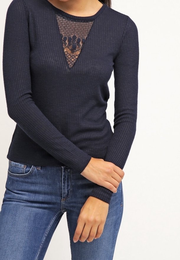 Haut marine à manches longues côtelé avec un détail en triangle en dentelle à l'encolure, associé à un jean en denim. Le tissu semble texturé et ajusté.