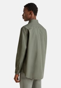 Camisa de manga larga en tejido verde olivo con una textura suave, con cuello abotonado y mangas con puños. Corte ajustado con dobladillo recto.