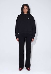 Black oversized hoodie with logo, paired with black fitted pants. Model wears maroon flats. Simple design, soft texture, no visible patterns.