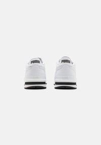 Baskets blanches en matériau lisse, avec des accents noirs sur la semelle et le logo "PUMA" sur le talon et la languette, présentant un design classique.