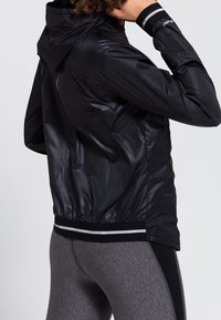 Czarna, lekka kurtka z kapturem, elastycznymi mankietami i pasem w białe paski. Gładka tekstura i dopasowany fason.