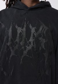 Sudadera con capucha negra con un diseño de cortes irregulares en un tono negro más oscuro, con una textura suave y un ajuste cómodo.