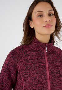 Chaqueta de forro polar con cremallera en rosa jaspeado y con un alto cuello, que presenta una cremallera de contraste y un tejido texturizado. Diseño ajustado y deportivo.