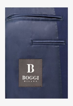 Tessuto blu navy con una superficie liscia e due tasche orizzontali. È visibile un'etichetta quadrata con "BOGGI MILANO" in bianco su uno sfondo grigio.