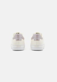 Baskets de couleur crème avec un accent mauve brillant sur le talon, semelle en caoutchouc blanche et silhouette épurée.