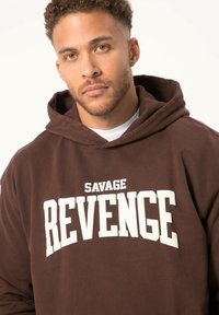 Felpa marrone in morbido cotone, con una grafica frontale in bianco che recita "SAVAGE REVENGE", dotata di un ampio cappuccio e polsini a coste.