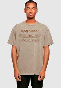 Hnědý oversized tričko s potiskem "Iron Maiden" a "Powerslave" ve zlaté barvě. Bavlněný materiál, krátké rukávy a kulatý výstřih.