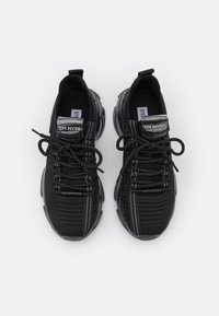 Zapatillas de malla negra con un patrón texturizado, que presentan cordones negros y franjas blancas reflectantes. Suela de goma con un diseño acolchado.