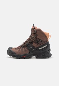 Brown hiking boot with a textured fabric upper, black rubber sole, and reinforced toe. Features prominent lacing and a contrasting orange heel tab.