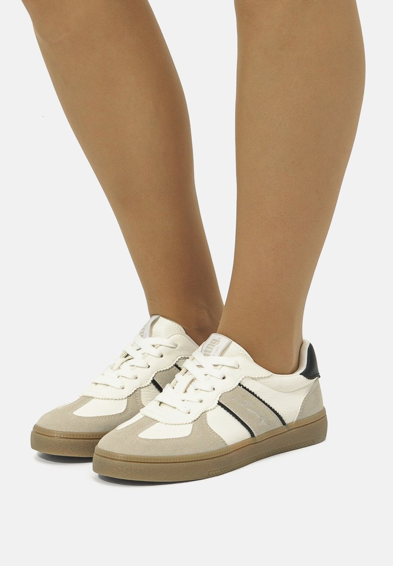 Sneaker mit einer Mischung aus Wildleder und Leder in Beige und Weiß, mit schwarzen Akzenten und klassischen weißen Schnürsenkeln. Robuste Gummisohle.