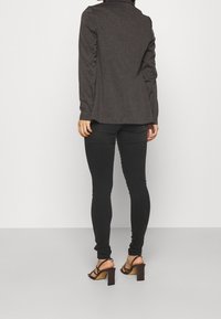 Donkergrijs shirt met lange mouwen en een kraag, gecombineerd met zwarte slim-fit broek en zwarte sandalen met dikke blokhakken.