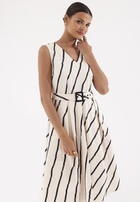 Sukienka bez rękawów w odcieniu kremowym z wyraźnymi czarnymi pionowymi paskami. Posiada dopasowaną talię z czarnym paskiem oraz plisowany dół.