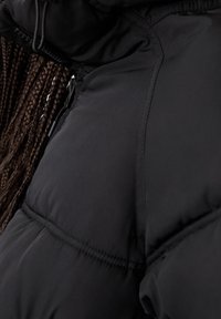 Sort pufferjakke-sektion med synlige sømme, glat tekstur og en lynlås. Viser et nærbillede af skulderområdet.