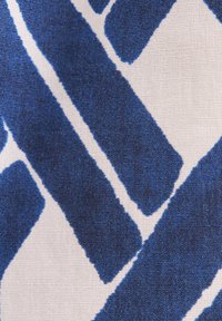 Gros plan d'un tissu avec un motif géométrique abstrait bleu et blanc présentant des formes diagonales et triangulaires irrégulières.