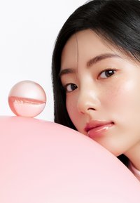 Masque à lèvres au collagène Abib PDRN dans un contenant rond et translucide de couleur rose, présenté aux côtés d'une surface lisse et rose, avec un gros plan sur les traits du visage.