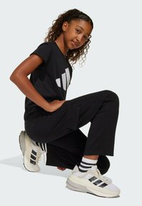 Svart t-shirt med vitt tryck, svarta byxor med fickor och vita sneakers med svarta ränder. Texturerad tyg; avslappnad passform.