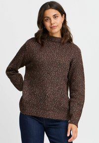 Suéter marrón de textura con cuello alto, que presenta un patrón de punto salpicado multicolor, combinado con vaqueros oscuros.