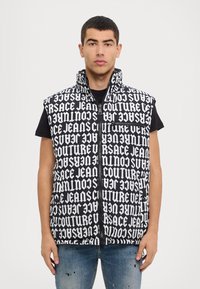 Gilet rembourré noir et blanc avec de grands motifs textuels répétés ; col haut, fermeture éclair à l'avant et poches sur les côtés ; coupe décontractée.
