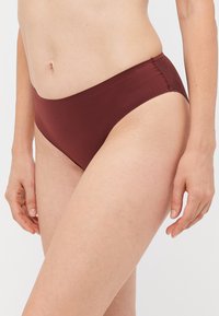 Burgundi színű, varrás nélküli bikini alsó. Simára csiszolt textúrával és modern, magas szabású lábszárrésszel rendelkezik. Rugalmas anyagból készült.