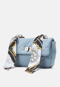 Quiltowana jasnoniebieska torebka z ekoskóry z zapięciem w złotym odcieniu oraz dwoma wzorzystymi chustami przywiązanymi do uchwytów.