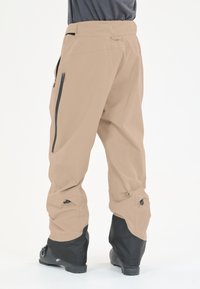 Beige Schnee-Hosendas mit schwarzen Unterschenkeln, ausgestattet mit Reißverschlusstaschen und verstellbaren Bündchen. Hergestellt aus einem leichten, wetterbeständigen Material.