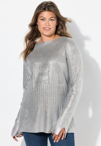 Suéter metálico plateado de manga larga con textura acanalada y un ajuste relajado. Presenta un cuello ancho y puños acampanados. Combinado con jeans azul oscuro.