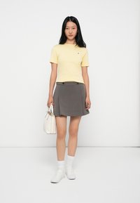 Żółta bluzka z krótkim rękawem, szara spódnica plisowana z podwójnymi guzikami, białe akcesoria, białe skarpetki i trampki. Prosty, czysty design.