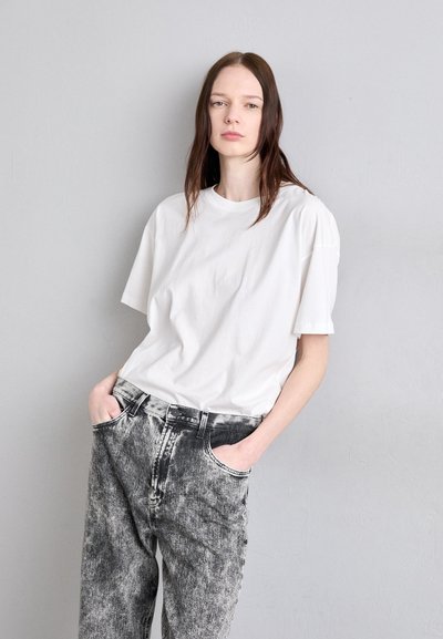 White short-sleeve t-shirt paired with faded black and gray jeans. The fabric is soft, with a relaxed fit and side pockets. Simple design.