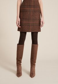 Minifalda de cuadro marrón con un acabado texturizado, combinada con medias oscuras marrones y botas de ante color canela hasta la rodilla con punta afilada.